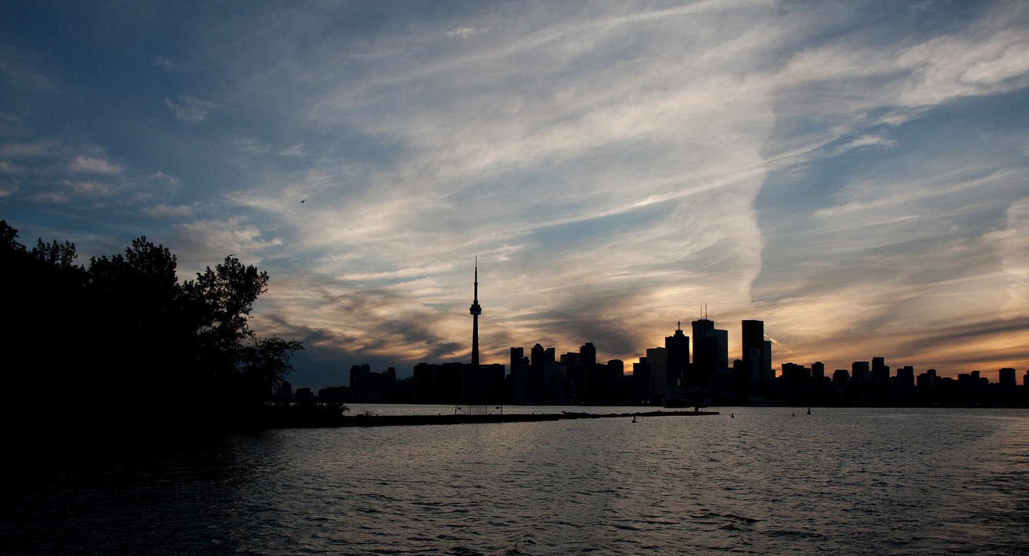 The Toronto skyline at dusk, the CN Tower silhouetted above the lake.
